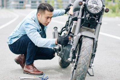 Homem agachado olhando para a bateria de moto. 